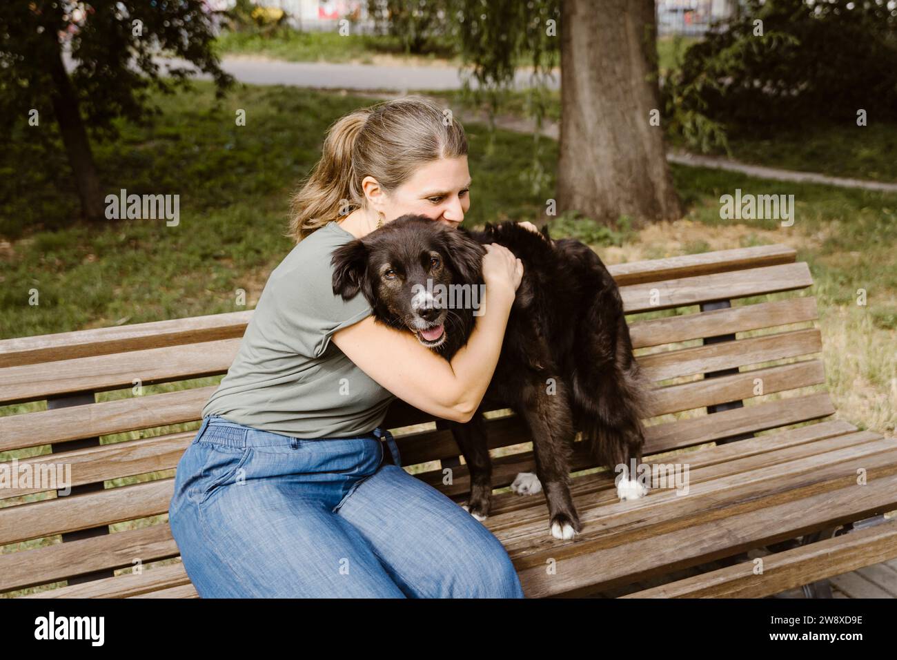 Reife Frau umarmt Hund auf Bank im Park Stockfoto