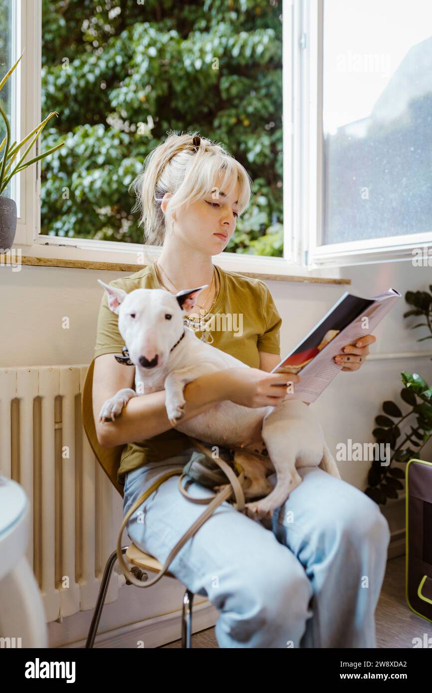 Blonde Frau mit Bullterrier Hund liest Zeitschrift auf Stuhl im Wartezimmer des Tierhauses Stockfoto