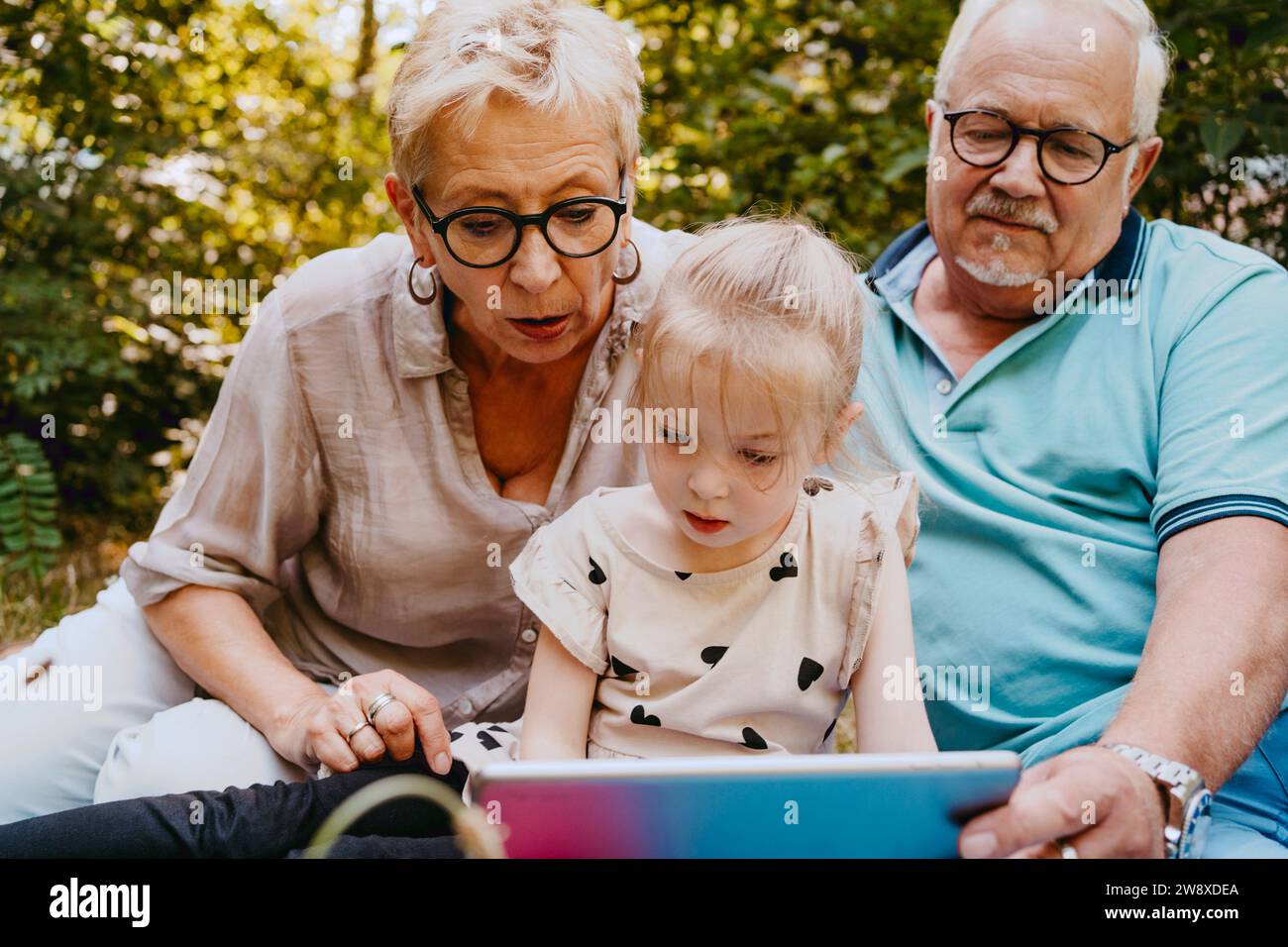 Enkelin liest Buch, während sie mit Großeltern im Park sitzt Stockfoto