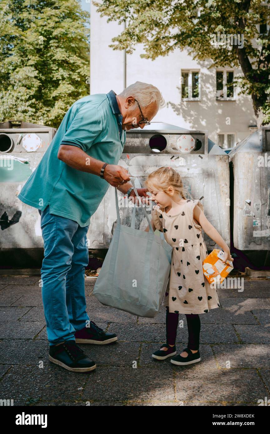 Großvater und Enkelin suchen in Tragetasche, während sie vor Mülltonnen auf der Straße stehen Stockfoto