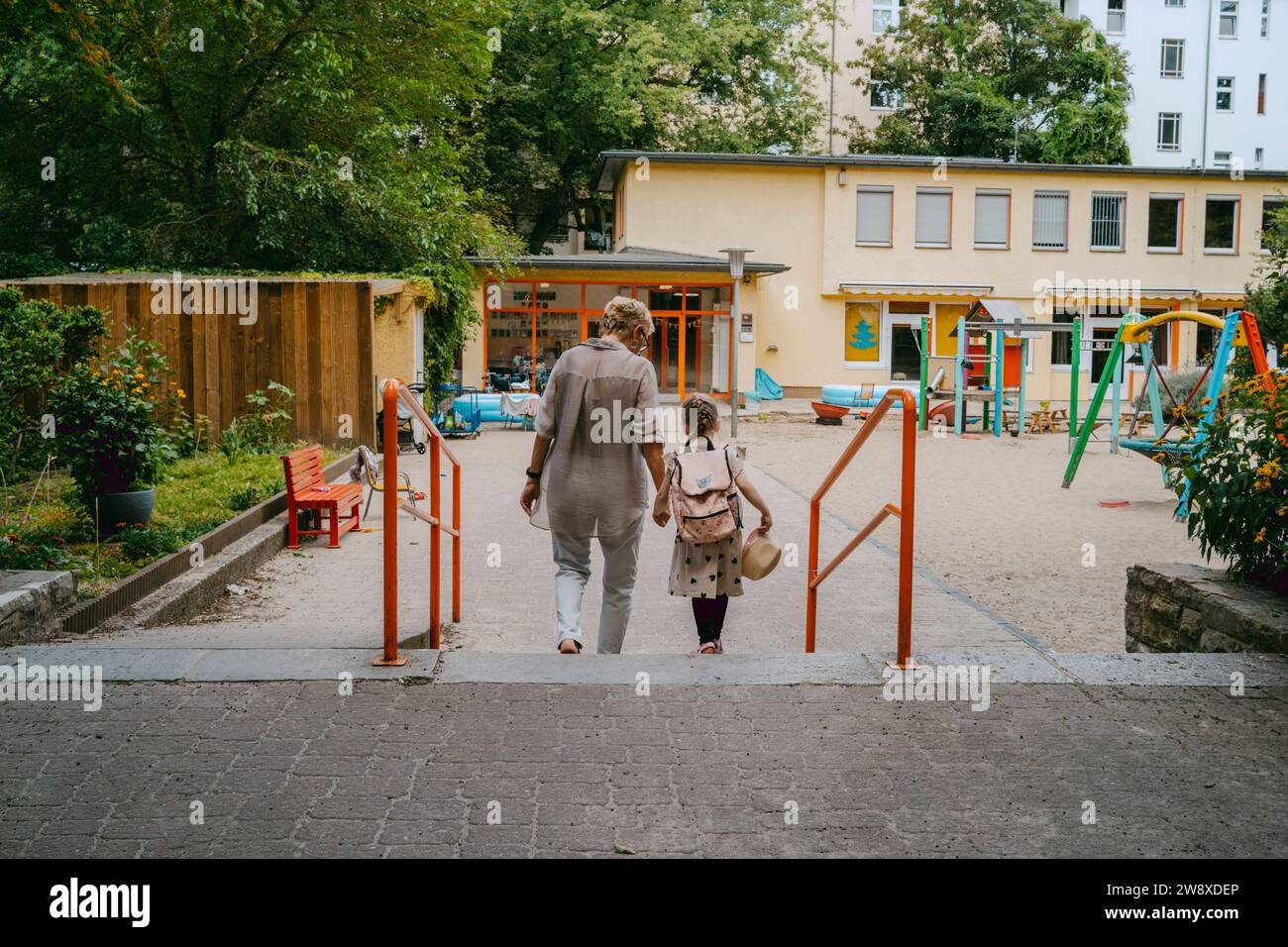 Rückansicht einer Seniorin mit Enkelin, die in Richtung Kindergarten geht Stockfoto