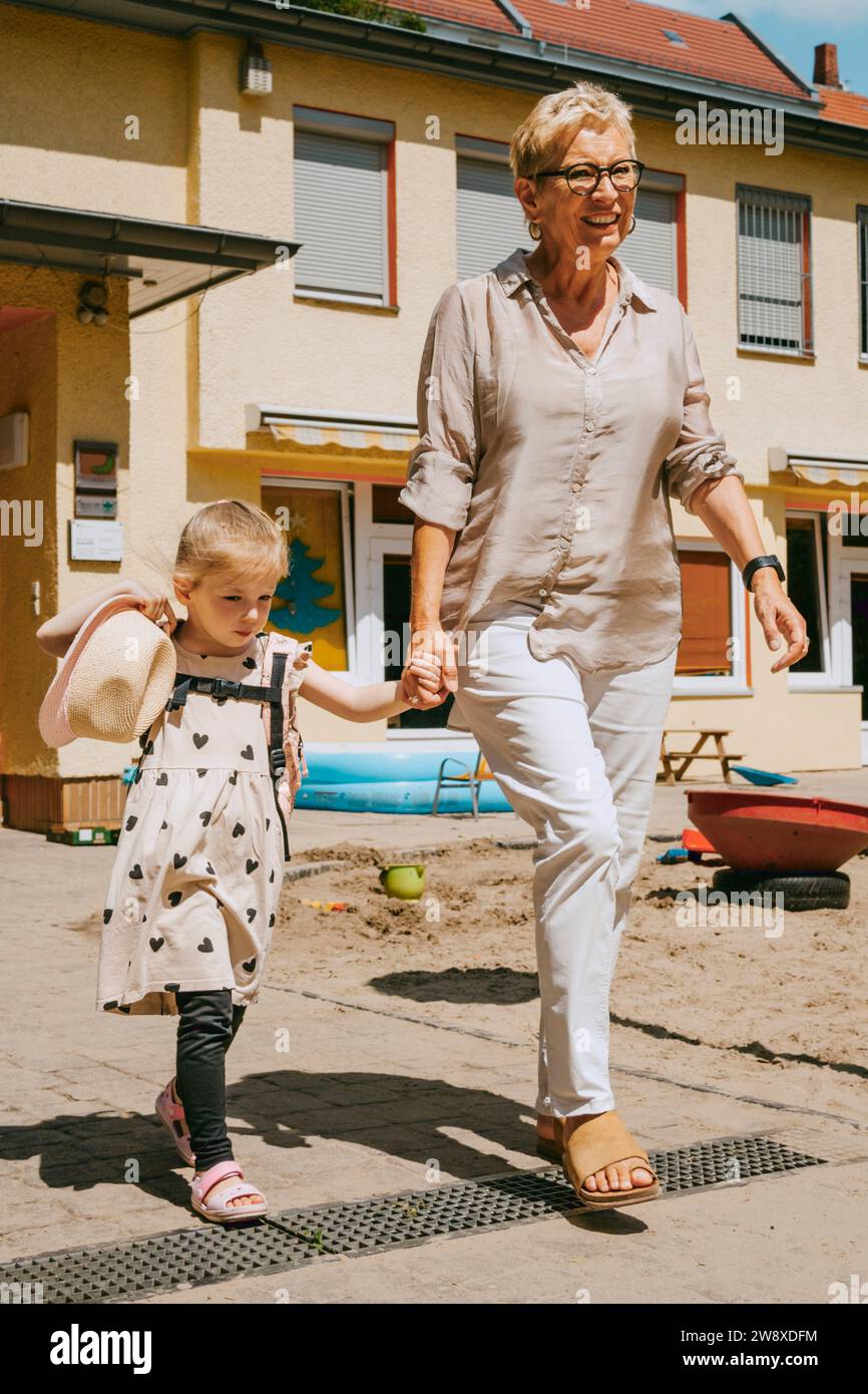 Großmutter mit Enkelin auf Fußweg vor dem Kindergarten Stockfoto