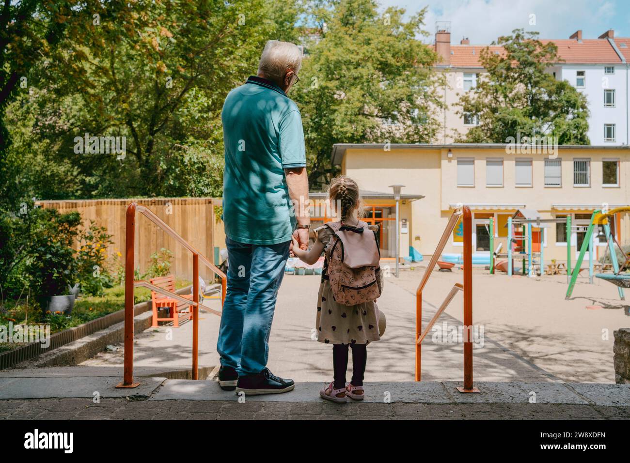 Seniorenmann mit Enkelin, die in der Nähe des Geländes im Kindergarten steht Stockfoto