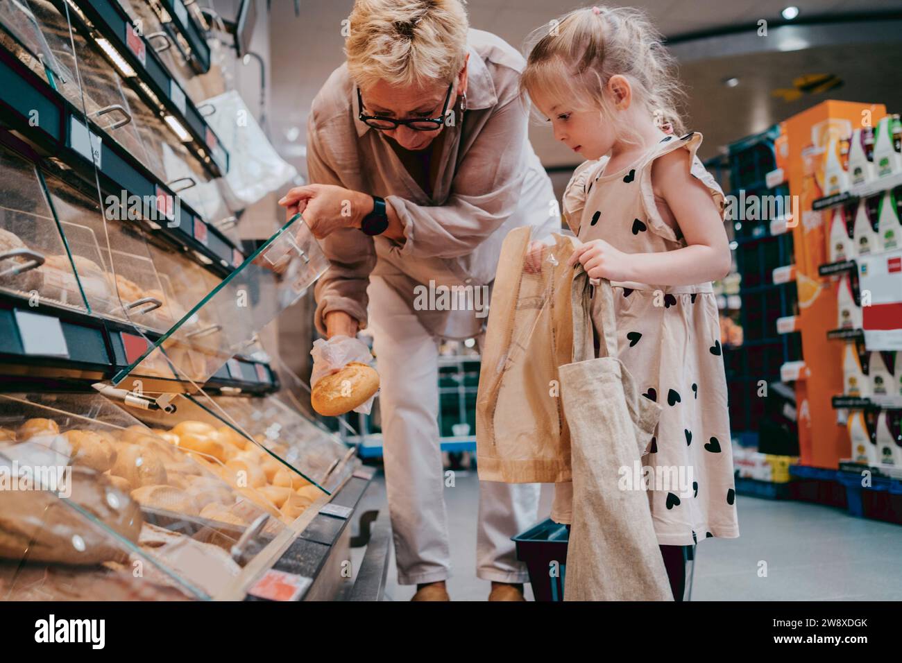 Seniorin kaufte Brot mit Enkelin, die Taschen im Supermarkt hält Stockfoto