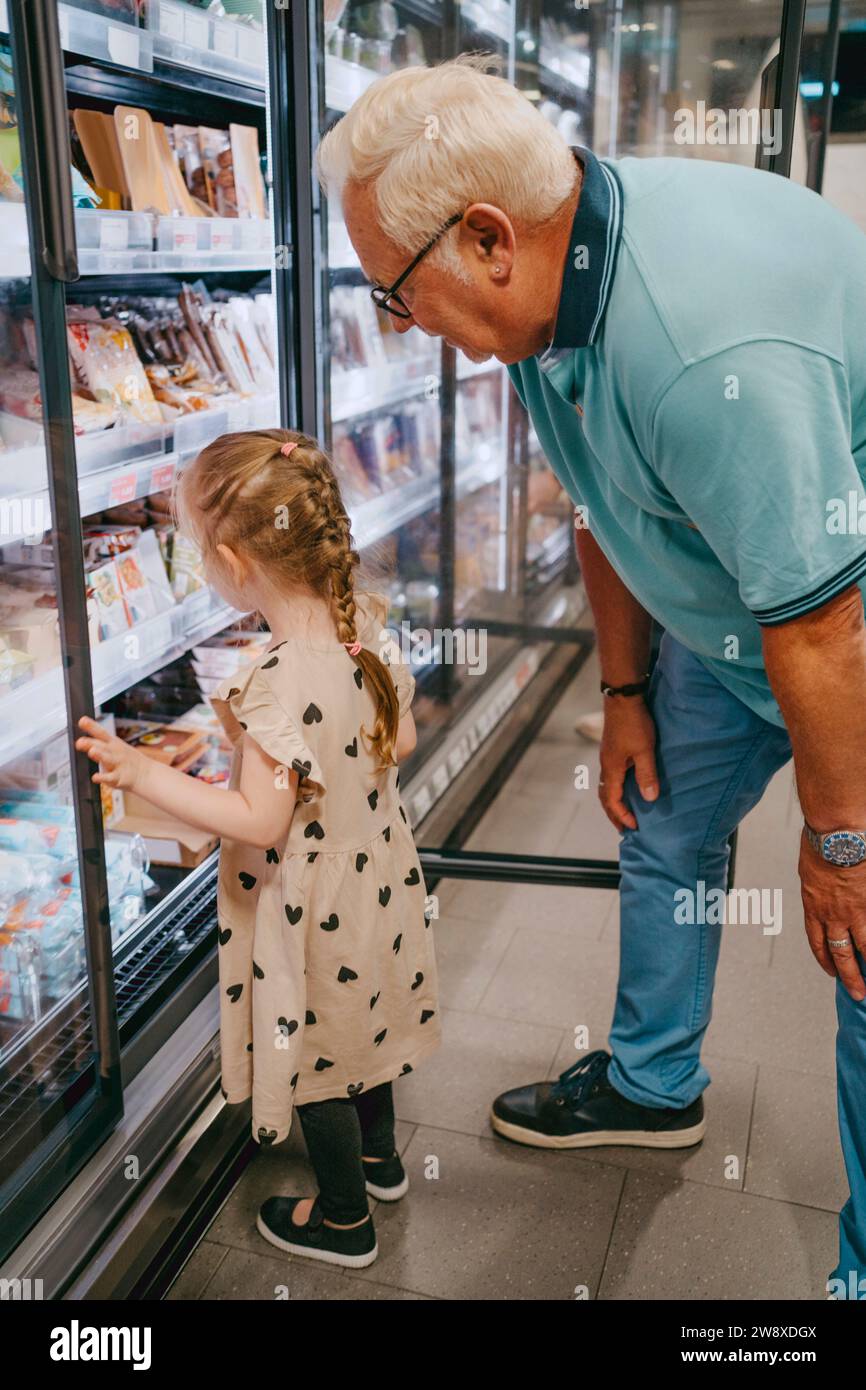 Ein Mädchen, das Tiefkühlkost kauft, während er mit Großvater im Supermarkt einkaufen geht Stockfoto