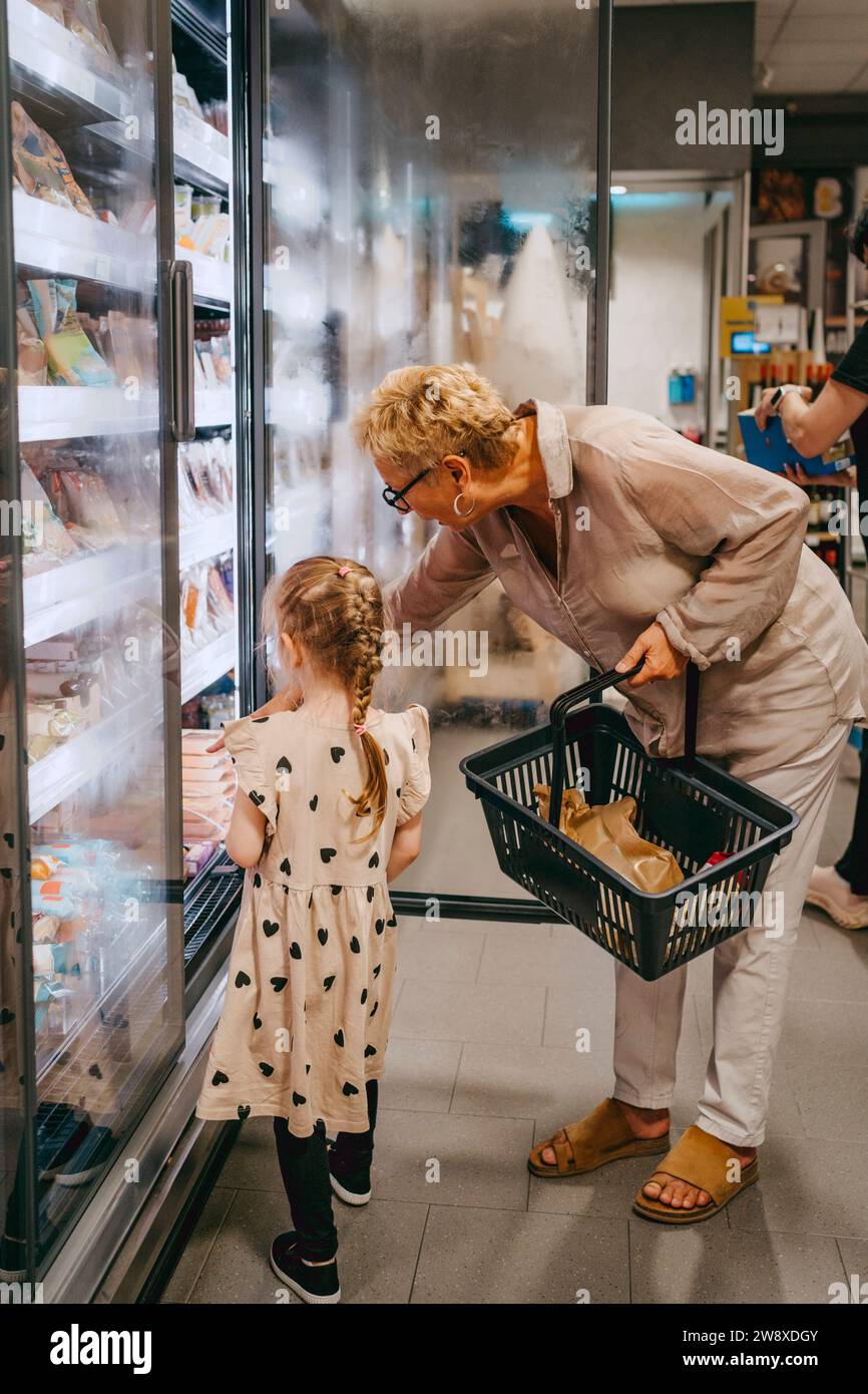 Ein Mädchen, das Tiefkühlkost aus dem Kühlbereich kauft, mit Großmutter im Supermarkt Stockfoto