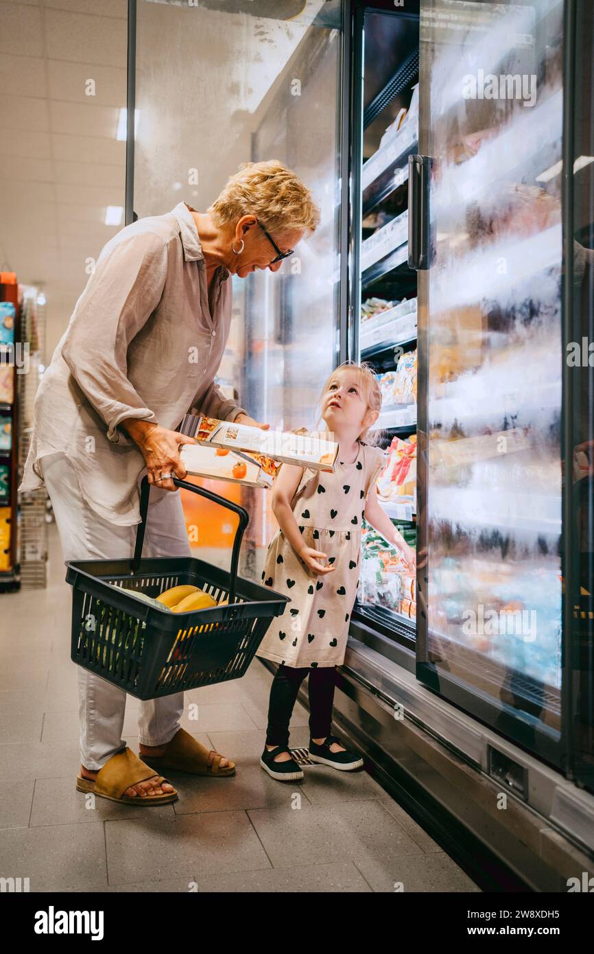 Seniorin, die einen Korb hält, während sie mit ihrer Enkelin im Laden einkaufen Stockfoto