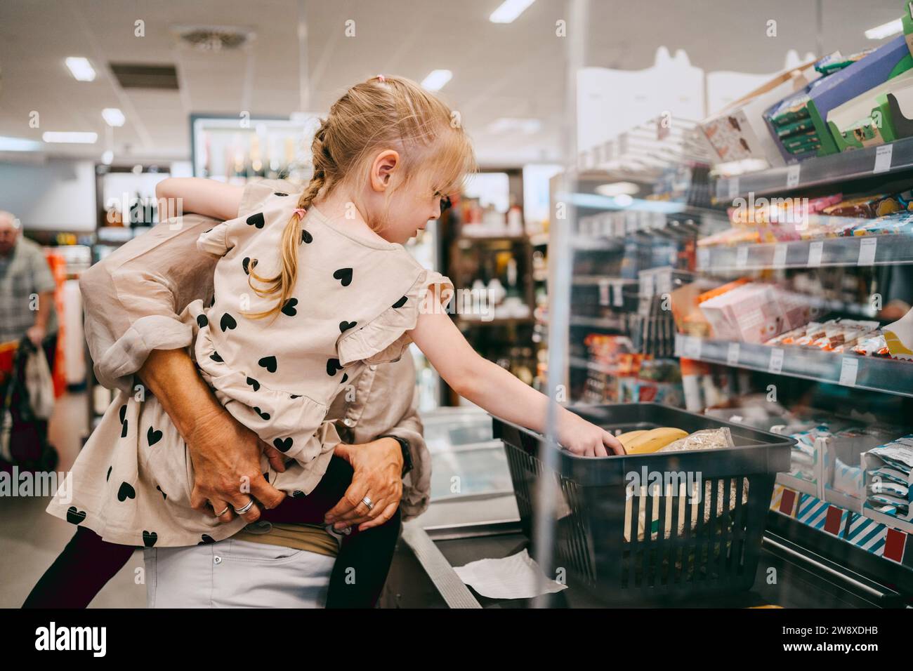 Eine ältere Frau, die Enkelin an der Kasse im Supermarkt trägt Stockfoto