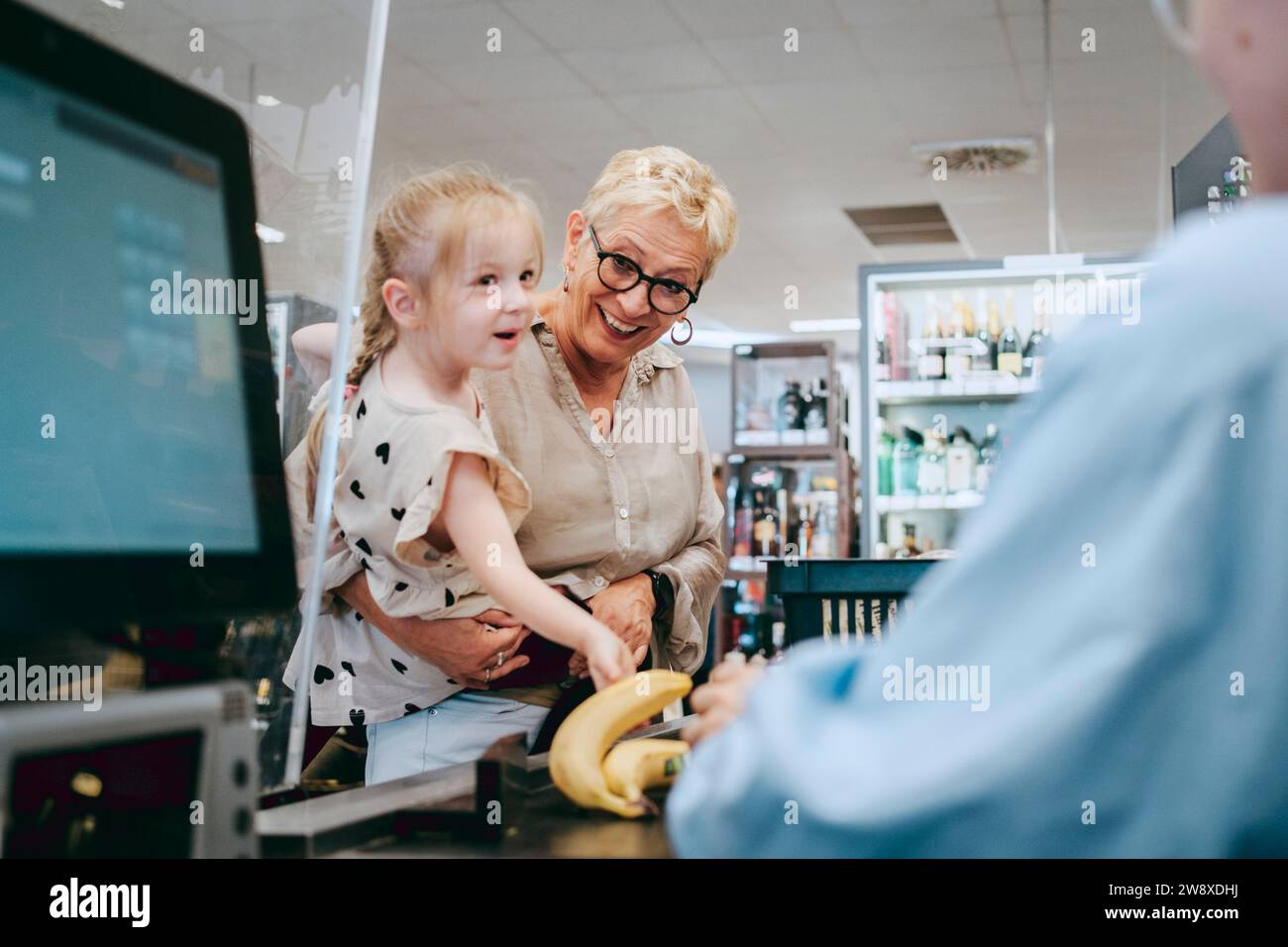 Glückliche Seniorin mit Enkelin in der Nähe der Kasse im Supermarkt Stockfoto