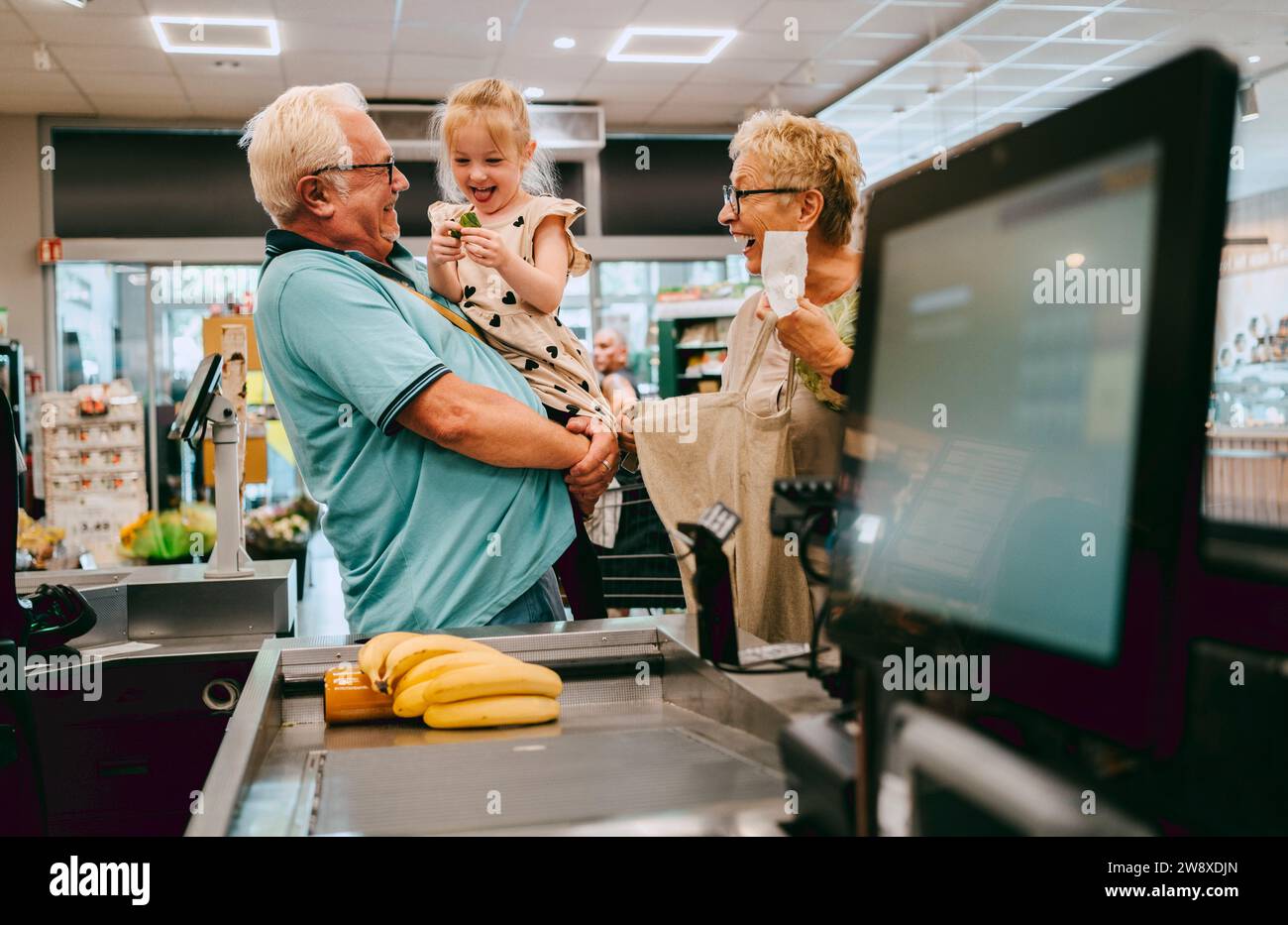Glückliche Enkelin, die Spaß mit den Großeltern beim Einkaufen im Supermarkt hatte Stockfoto