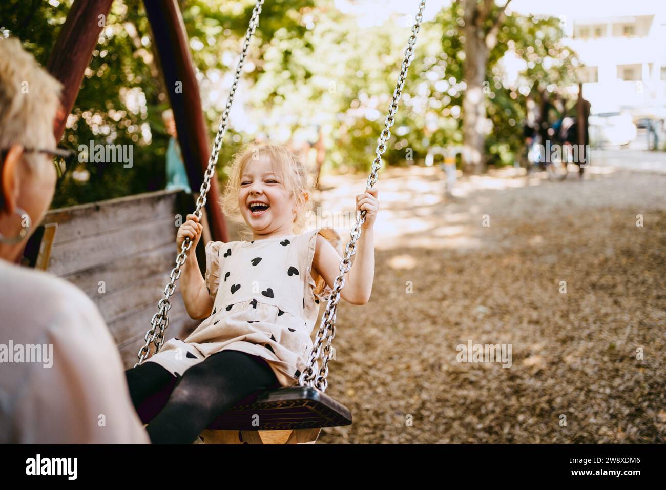 Glückliches Mädchen lacht, während es mit Großmutter im Park auf der Schaukel spielt Stockfoto