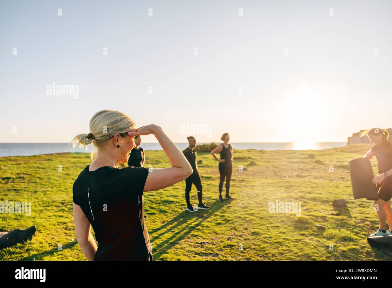 Frau schirmt Augen beim Gruppentraining an sonnigen Tag am Strand ab Stockfoto