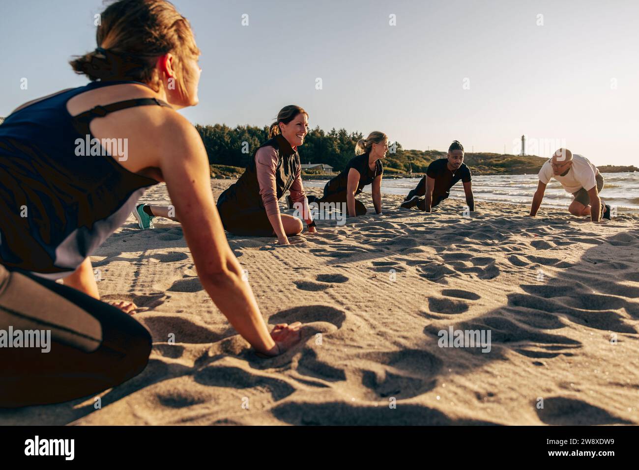 Lächelnde Ausbilderin, die mit dem Team am Strand am Strand Stretching macht Stockfoto