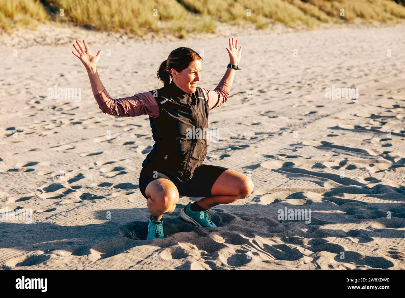 Reife weibliche Ausbilderin erklärt die Körperhaltung beim Hocken auf Sand am Strand Stockfoto