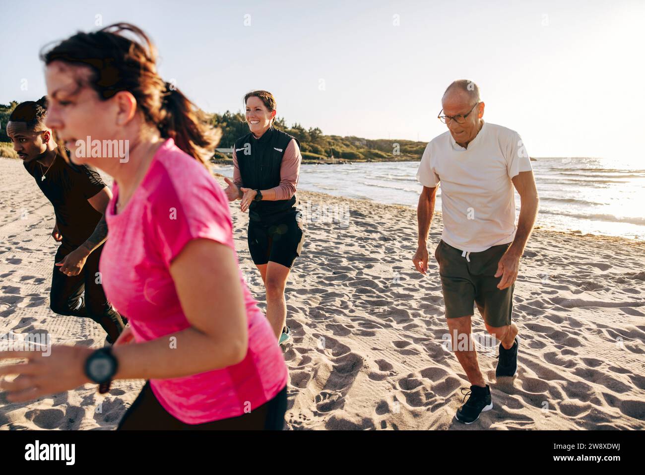 Lächelnde weibliche Ausbilderin, die das Team während des Gruppentrainings am Strand anfeuert Stockfoto