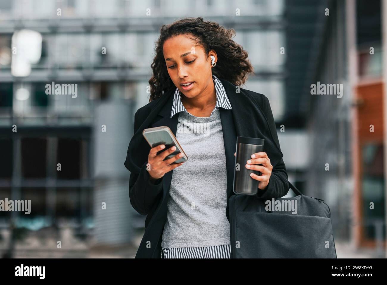 Geschäftsfrau, die ihr Smartphone benutzt, während sie einen isolierten Getränkebehälter hält Stockfoto