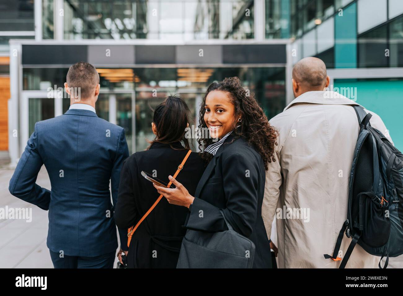 Seitenporträt einer lächelnden Geschäftsfrau, die mit Kollegen vor dem Gebäude über die Schulter schaut Stockfoto