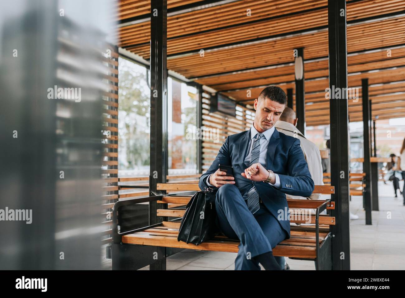Geschäftsmann überprüft die Zeit, während er auf der Bank an der Bushaltestelle sitzt Stockfoto