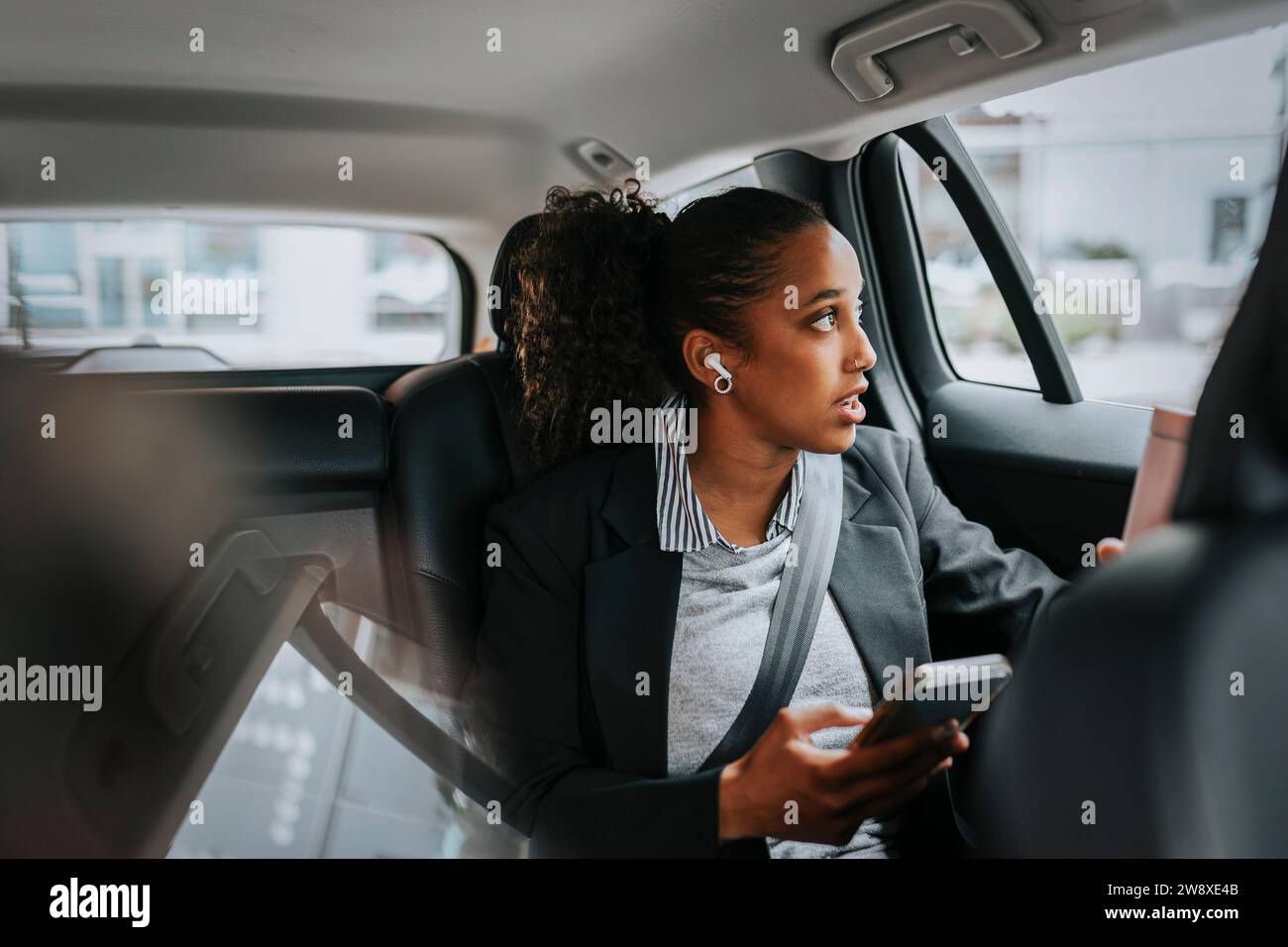 Geschäftsfrau, die durch das Fenster schaut und mit dem Smartphone spricht, während sie im Auto sitzt Stockfoto