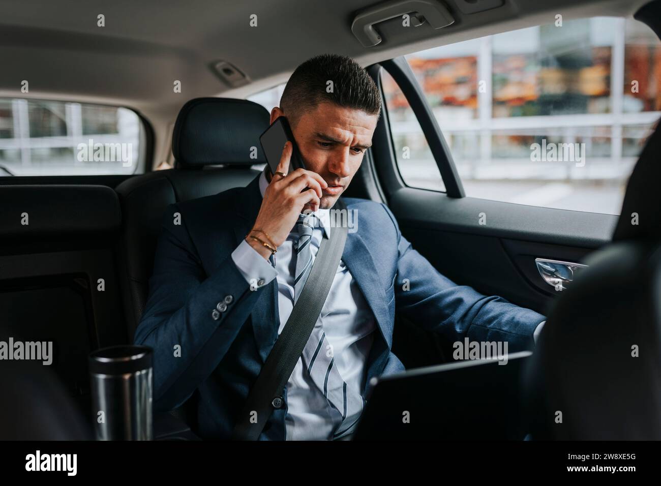 Geschäftsmann, der mit dem Smartphone spricht, während er mit dem Laptop im Auto sitzt Stockfoto