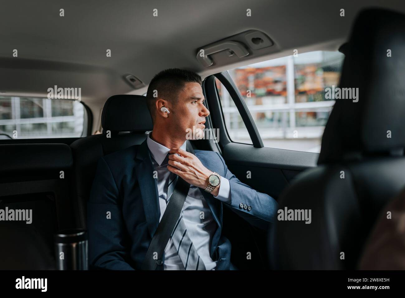 Geschäftsmann passt Krawatte an und schaut durch das Fenster, während er im Auto sitzt Stockfoto