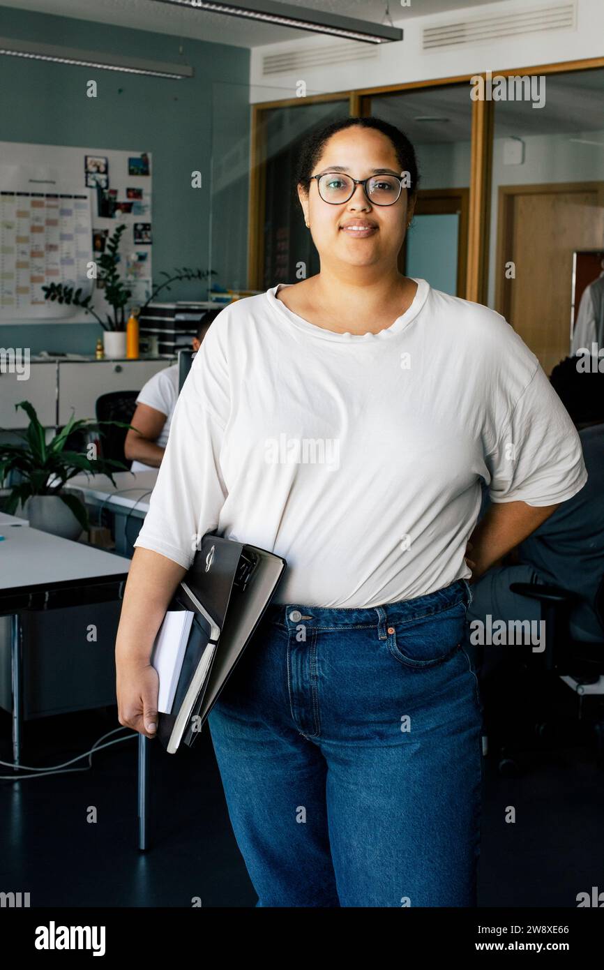 Porträt einer Computerprogrammiererin, die Dateien hält, während sie im Büro steht Stockfoto
