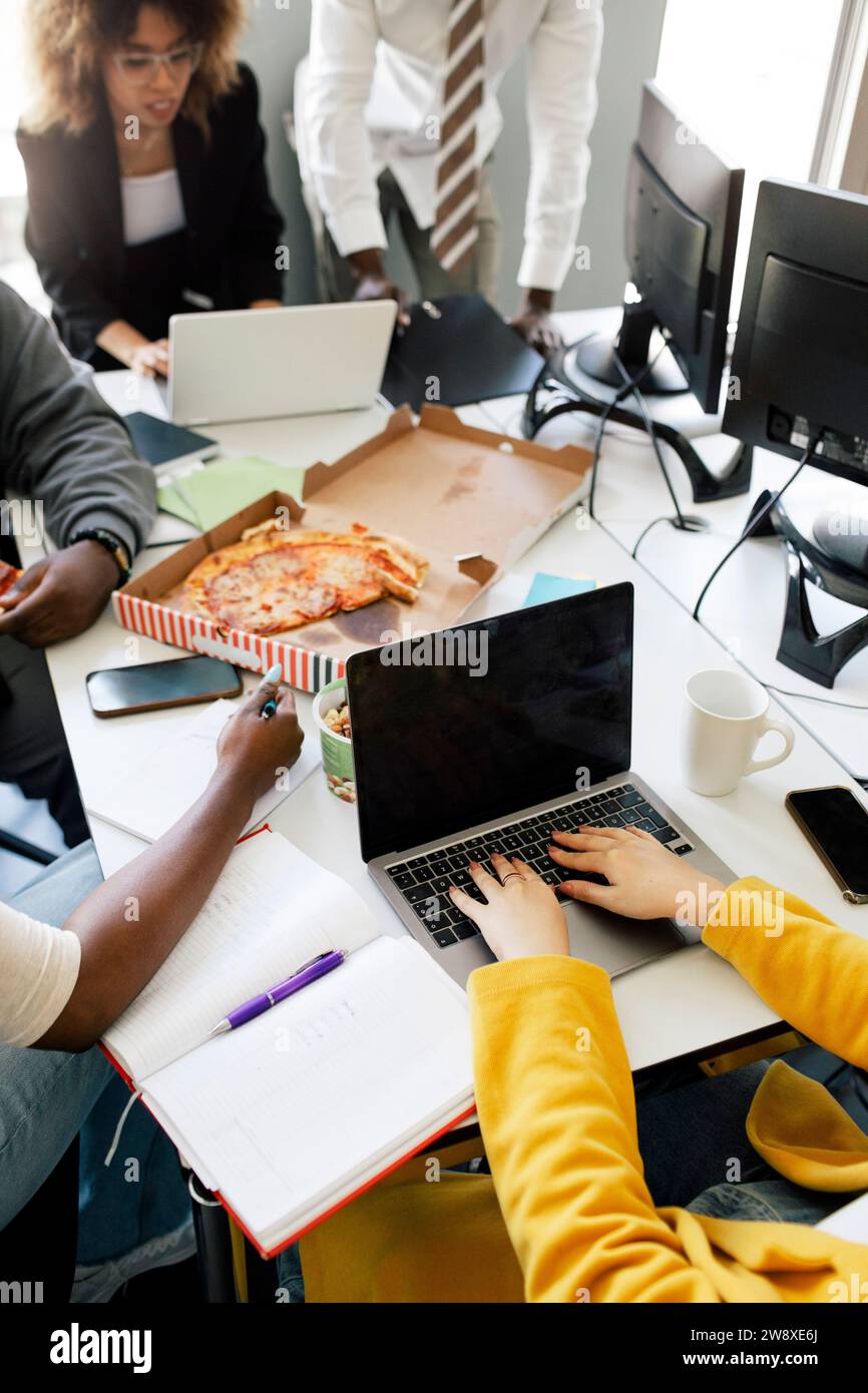 Hochwinkelansicht des Codierens von Unternehmerinnen auf einem Laptop bei Besprechungen mit Kollegen im Büro Stockfoto