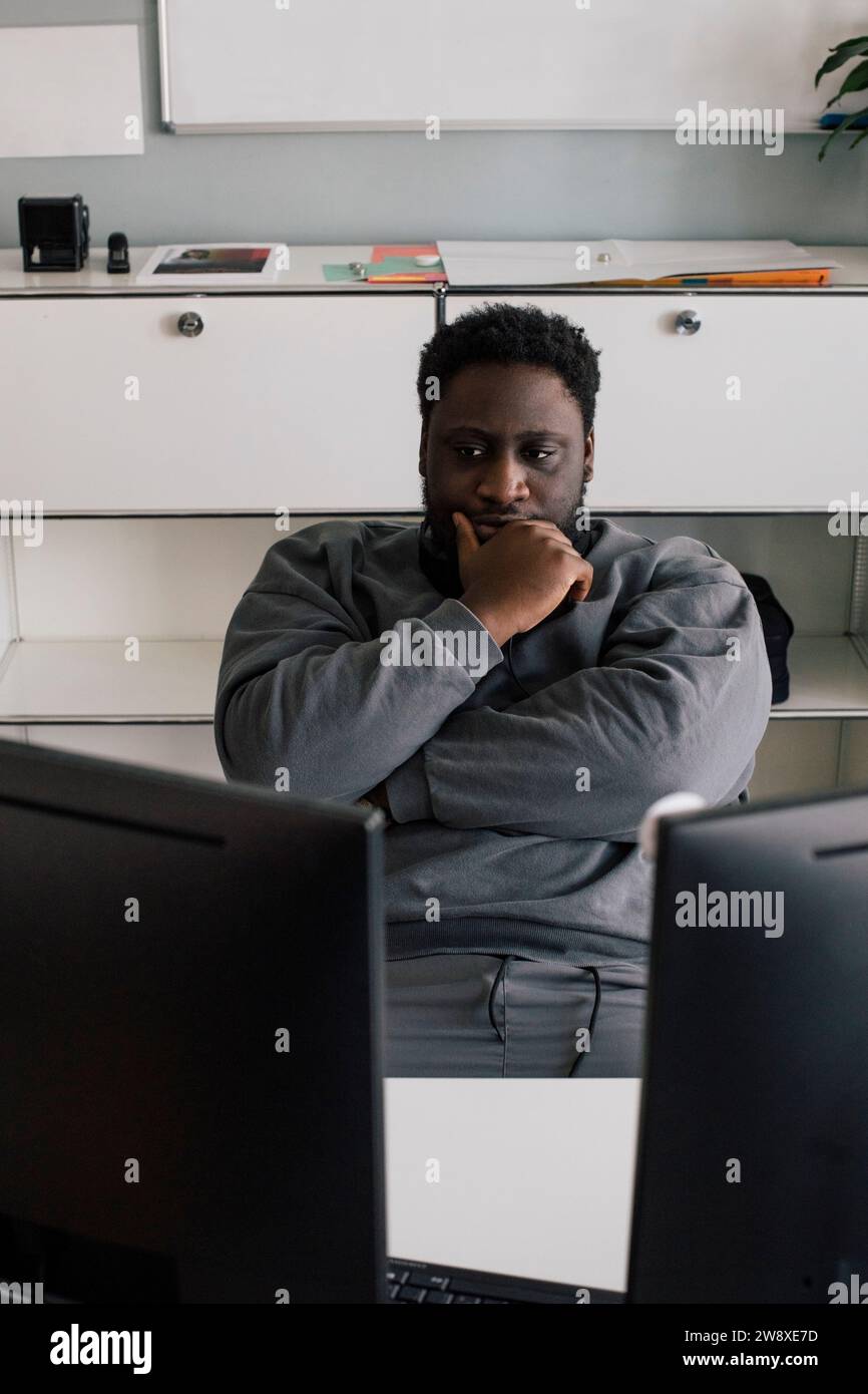 Männlicher Unternehmer mit Hand am Kinn, der im Büro sitzt Stockfoto