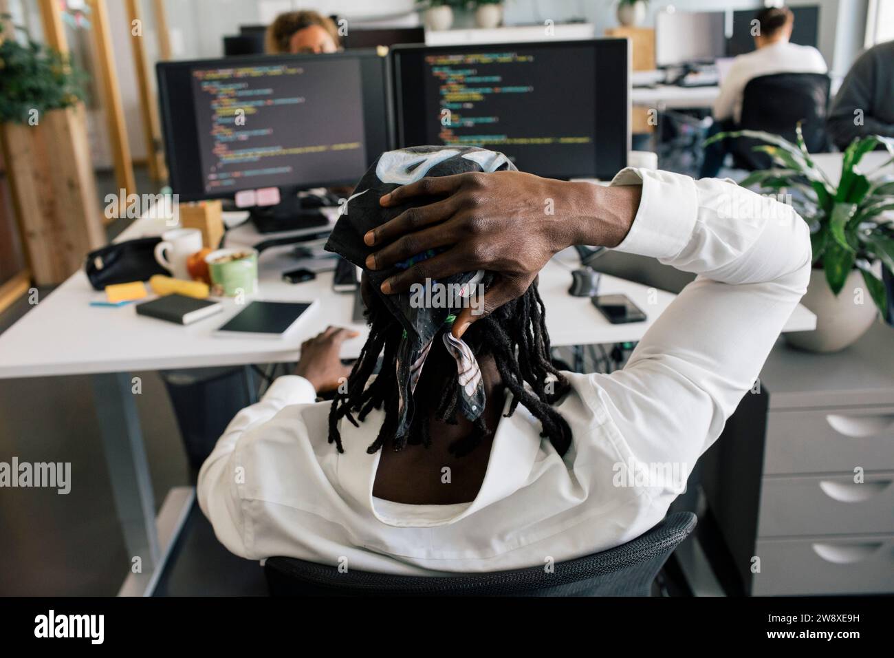 Rückansicht eines männlichen Computerprogrammierers, der im Büro mit dem Kopf in der Hand sitzt Stockfoto