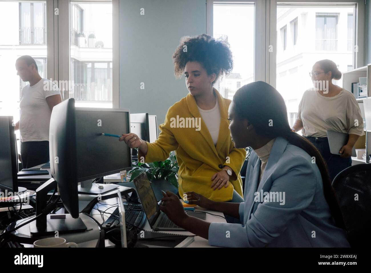 Geschäftsfrau erklärt Codierung einer Kollegin, die am Schreibtisch im Büro sitzt Stockfoto