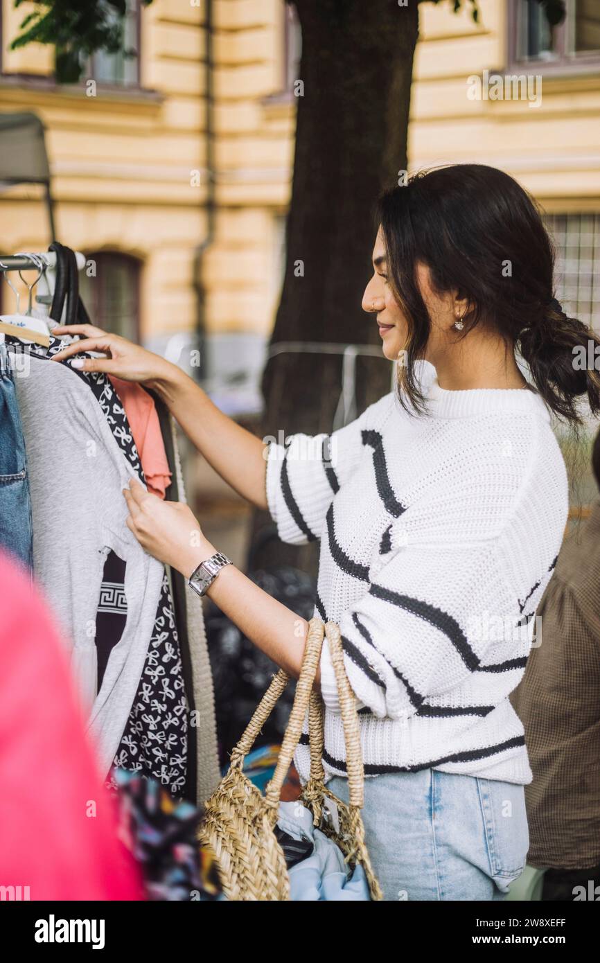 Seitenansicht einer Frau, die beim Einkaufen auf dem Flohmarkt ein Kleid aus dem Regal auswählte Stockfoto