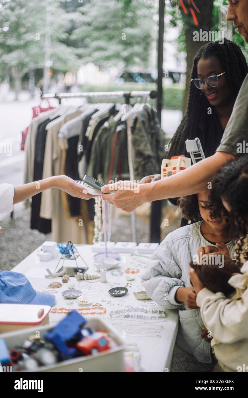 Mann, der kontaktlos bezahlt, während er in der Nähe des Verkaufsstandes auf dem Flohmarkt einkaufen geht Stockfoto