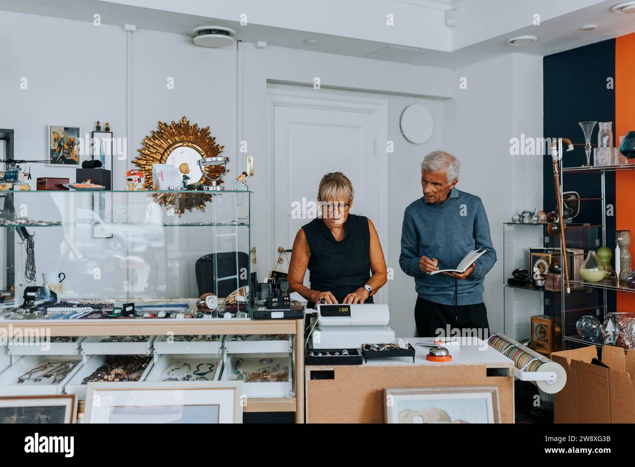 Männliche und weibliche Besitzer stehen an der Kasse, während sie in einem Antiquitätenladen arbeiten Stockfoto