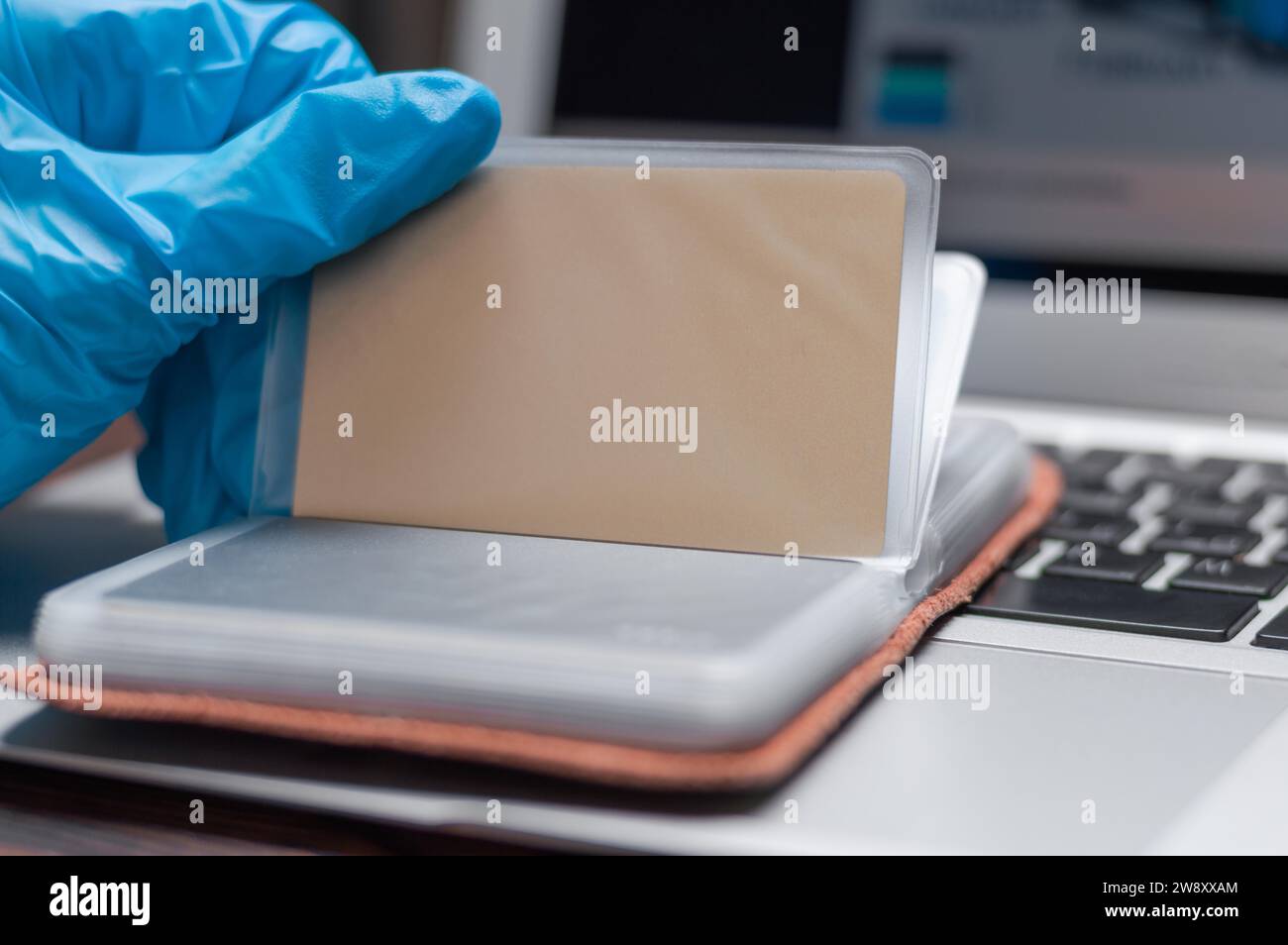 Bild der Hände in medizinischen Handschuhen auf dem Hintergrund eines Laptops. Die Frau hält eine Plastikkarte und gibt die Nummer auf der Website ein. Online Stockfoto