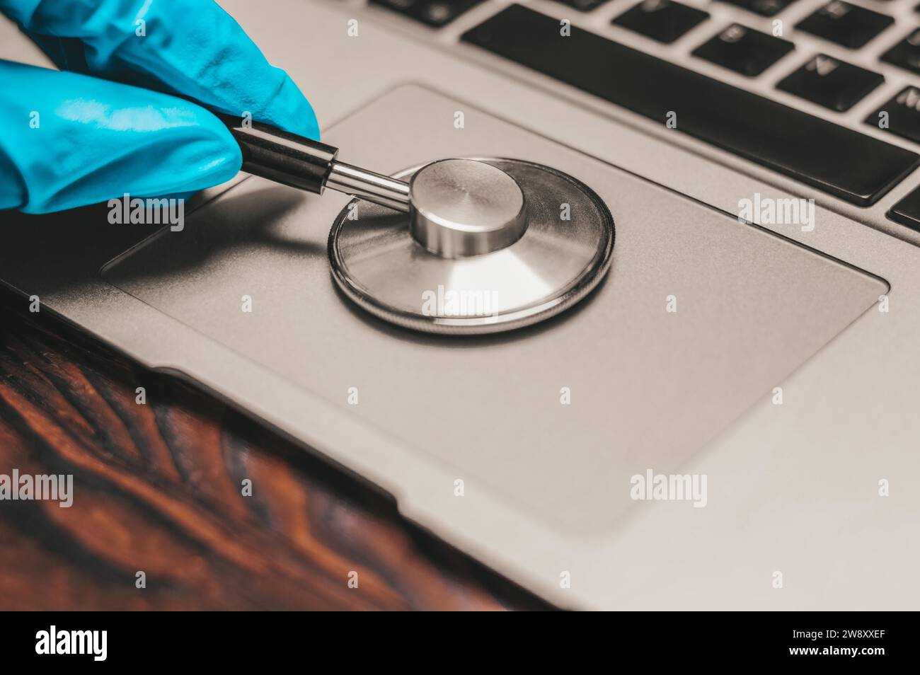 Bild der Hände in medizinischen Handschuhen. Der Techniker wendet ein Stethoskop an einem Laptop an. Computerwerkstatt-Konzept. Gemischte Medien Stockfoto