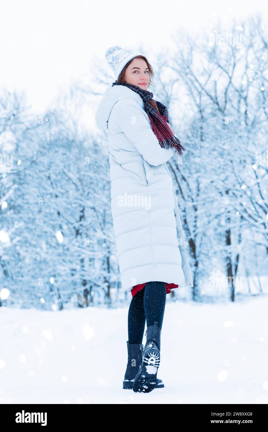 Charmante große Frau posiert vor dem Hintergrund eines schneebedeckten Parks mit einem Buch in der Hand. Weihnachtsferien-Konzept. Gemischte Medien Stockfoto