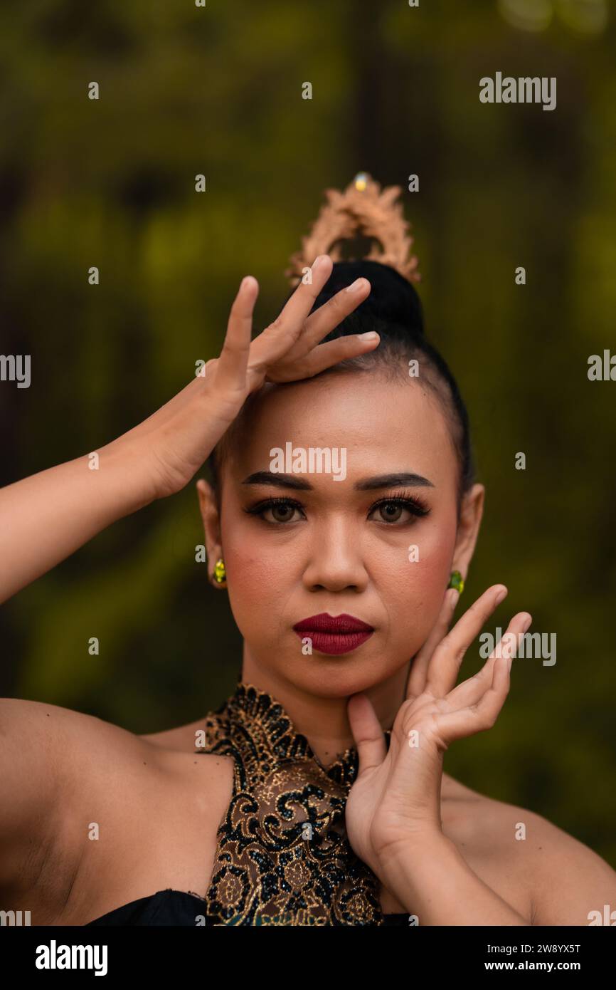 Tapferes Gesicht einer asiatischen Frau in einem traditionellen grünen Kostüm mit goldenen Accessoires am Körper während des Wettkampfes bei einem Tanzfestival vor der Tür Stockfoto