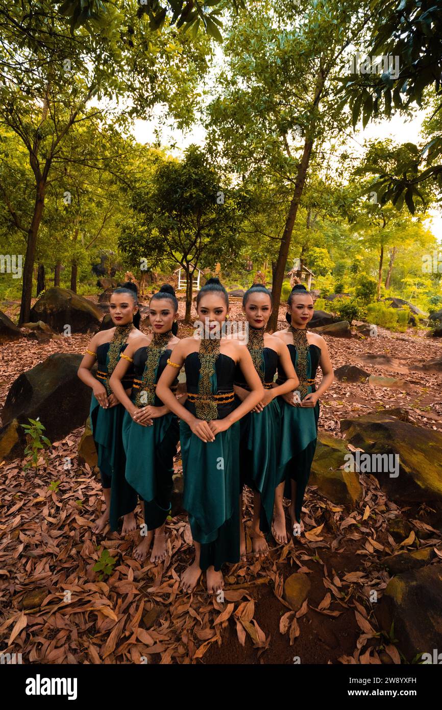 Eine große Aufnahme einer asiatischen Frau, die zusammen im Wald steht, während sie ein grünes Tanzkostüm mit toten Blättern im Hintergrund trägt Stockfoto