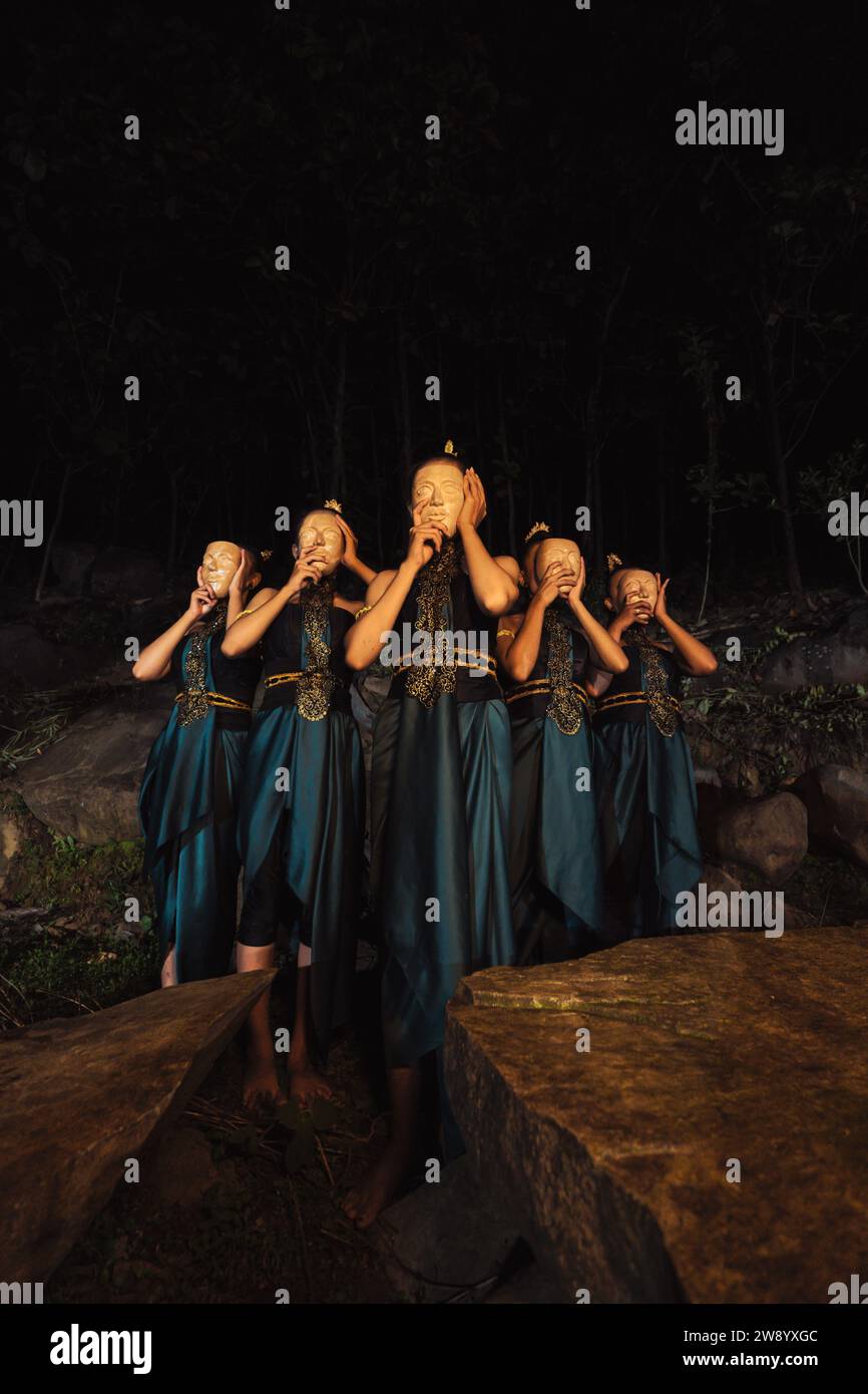 Eine Gruppe indonesischer Frauen, die eine braune Holzmaske in einem grünen Rock zwischen dem Felsen im Wald tragen Stockfoto