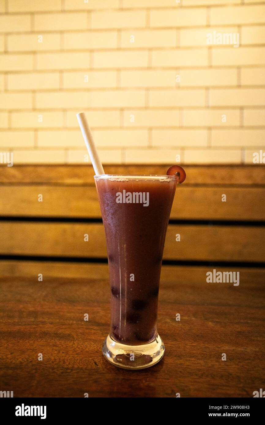 Ein Nahfoto eines Glases lila Flüssigkeit, wahrscheinlich Traubensaft, mit einer einzigen grünen Traube darüber. Das Glas sitzt auf einem dunklen Holztisch, und Stockfoto