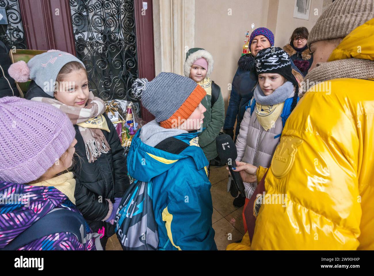 Reporter, der Kinder in der Nähe von Szopka (Weihnachtskrippe) interviewt, die sie in ihrer Grundschule gemacht haben, auf der Eröffnung des jährlichen Wettbewerbs im Dezember, der Veranstaltung, die in die Liste des UNESCO-Weltkulturerbes aufgenommen wurde, in den Arkaden von Sukiennice (Tuchhalle), dem Hauptmarkt in Kraków, Polen Stockfoto
