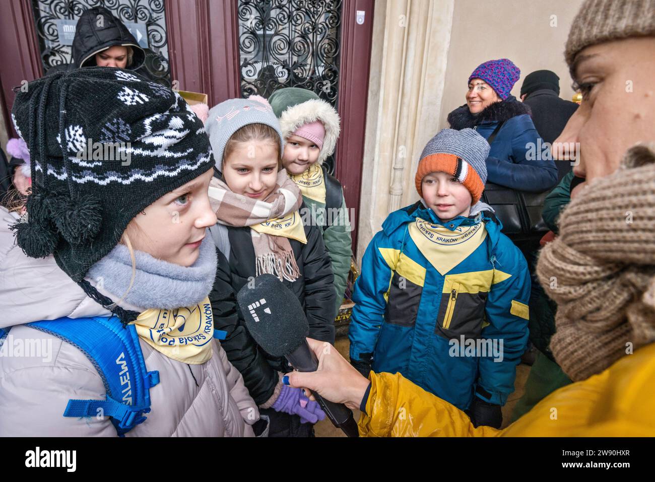 Reporter, der Kinder in der Nähe von Szopka (Weihnachtskrippe) interviewt, die sie in ihrer Grundschule gemacht haben, auf der Eröffnung des jährlichen Wettbewerbs im Dezember, der Veranstaltung, die in die Liste des UNESCO-Weltkulturerbes aufgenommen wurde, in den Arkaden von Sukiennice (Tuchhalle), dem Hauptmarkt in Kraków, Polen Stockfoto