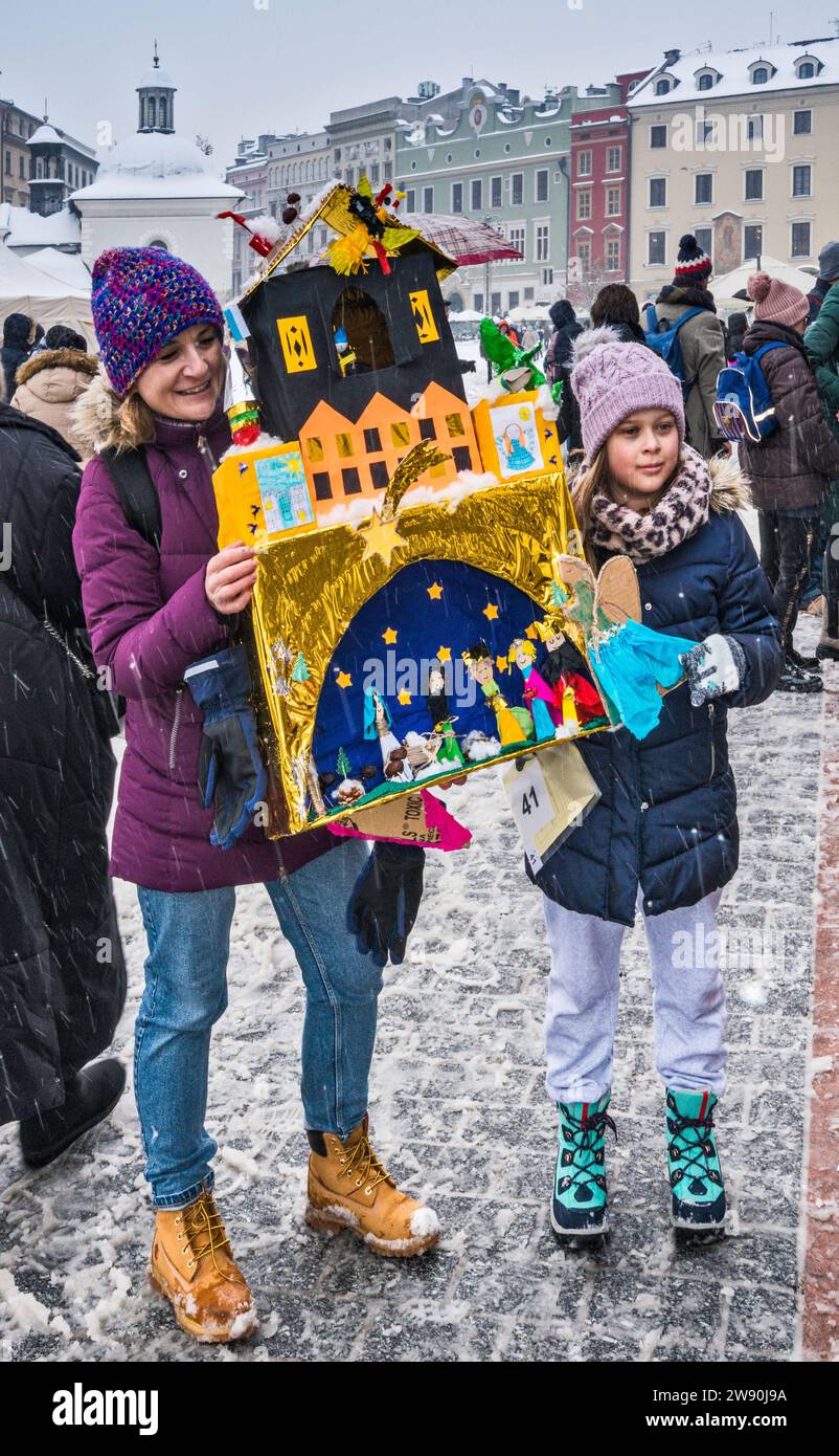 Mutter und Tochter mit Szopka (Weihnachtskrippe) Tochter, die bei Eröffnung des jährlichen Wettbewerbs im Dezember in die Liste des UNESCO-Weltkulturerbes aufgenommen wurde, in den Arkaden von Sukiennice (Tuchhalle), Hauptmarkt, Kraków, Polen Stockfoto