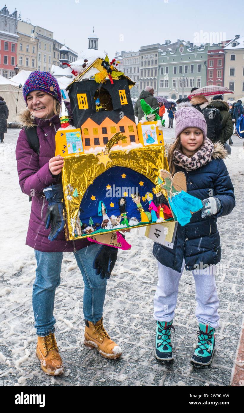 Mutter und Tochter mit Szopka (Weihnachtskrippe) Tochter, die bei Eröffnung des jährlichen Wettbewerbs im Dezember in die Liste des UNESCO-Weltkulturerbes aufgenommen wurde, in den Arkaden von Sukiennice (Tuchhalle), Hauptmarkt, Kraków, Polen Stockfoto