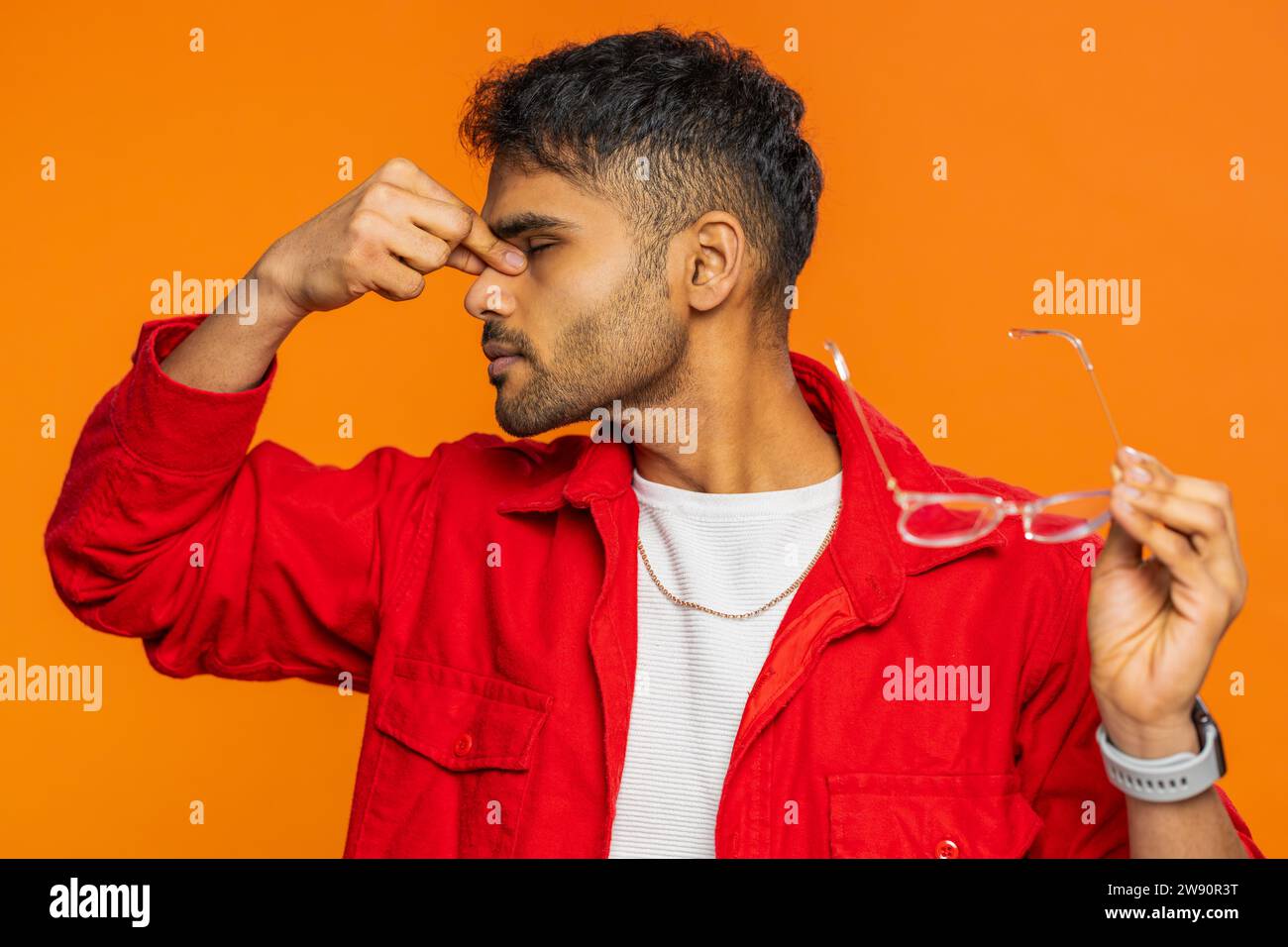 Erschöpfter, müder indischer junger Mann zieht die Brille aus, spürt Augenschmerzen, ist überlastet Burnout von langer Arbeit. Verschlafener, erschöpfter Arabianer, der die Augen isoliert auf orangefarbenem Hintergrund innen reibt Stockfoto