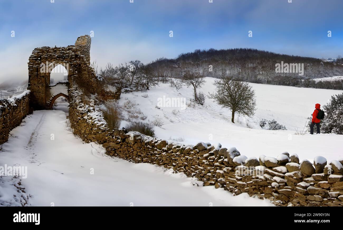 Ein Wanderer auf einem schneebedeckten Hügel in der Nähe der Ruinen einer Burg in den Highlands von Schottland. Stockfoto