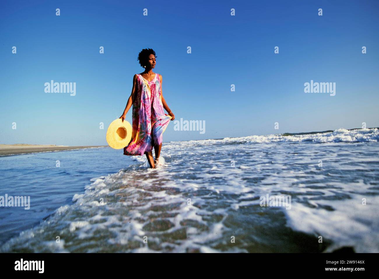 Eine Frau mit Strohhut, die allein durch die einsame Brandung an einem verlassenen Strand in North Carolina geht Stockfoto