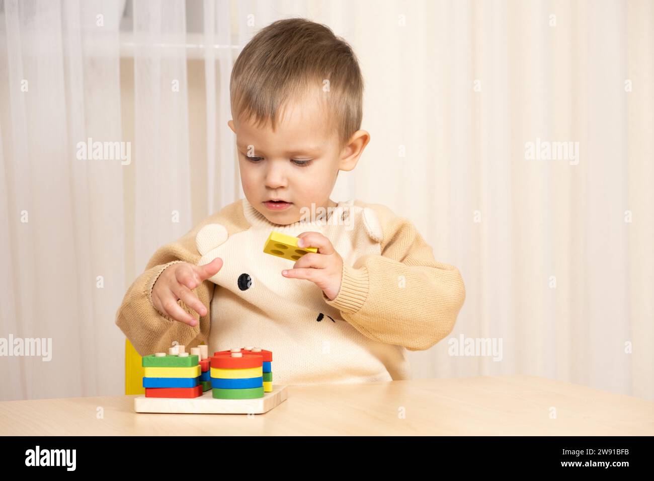 Ein zweijähriger Junge spielt mit Holzspielzeug, um Logik und Motorik zu entwickeln Stockfoto