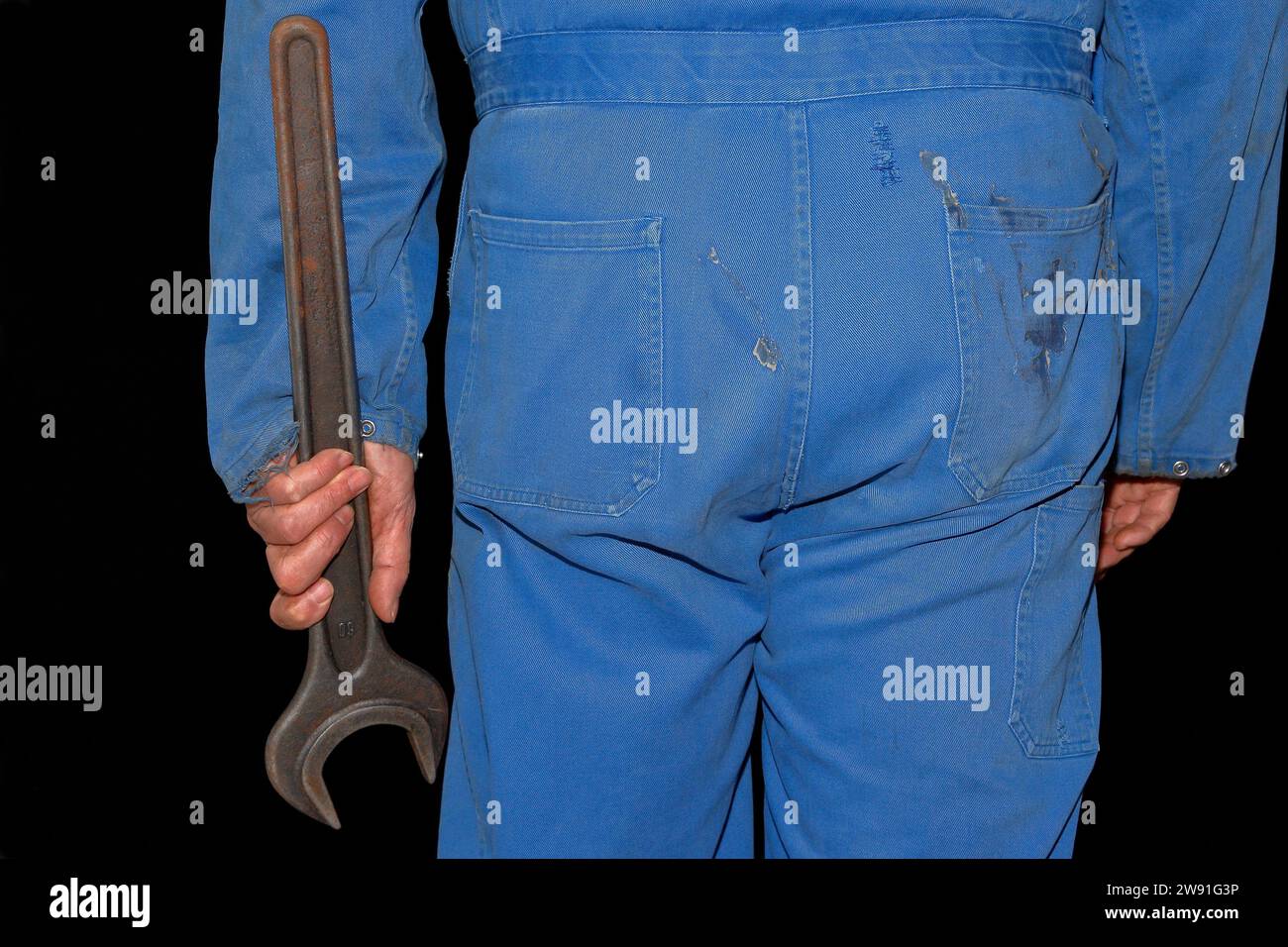 Handwerker in blauem Overall mit 60-mm-Maulschlüssel, Rückansicht. Ein Symbol des rückläufigen deutschen Handwerks. Stockfoto