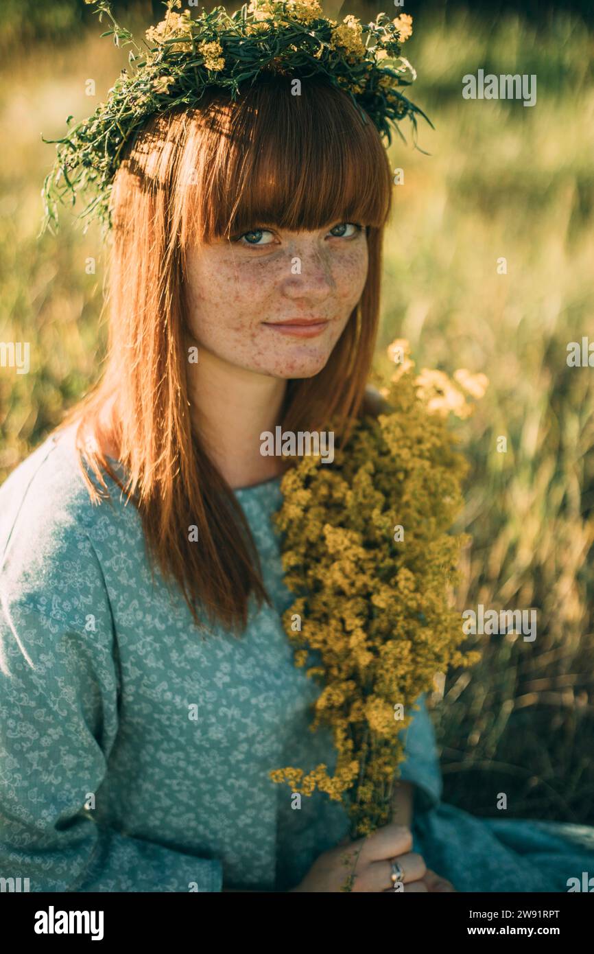 Junge Rothaarige Frau, die einen Blumenkranz auf dem Feld trägt Stockfoto